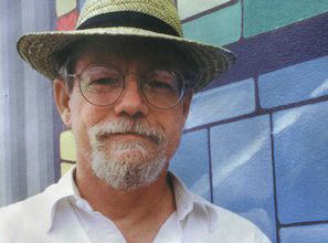 Portrait of mural artist Robert Dafford smiling and holding a paint pallette and brush.