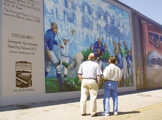 Two man standing in front of and viewing a mural of Portsmouth football team called the Spartans.
